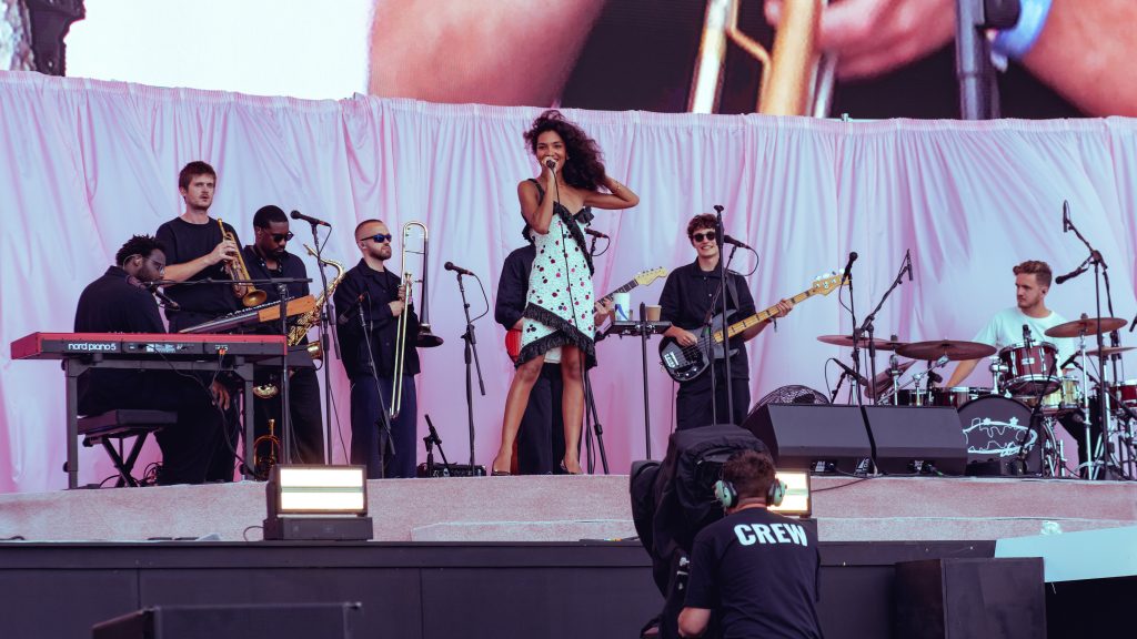 Olivia Dean zingt op het podium tijdens een live optreden, met microfoon in de hand